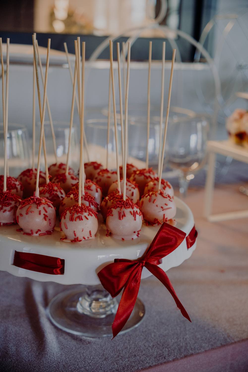 Cake popsy z czerwoną posypką na paterze z czerwoną kokardą